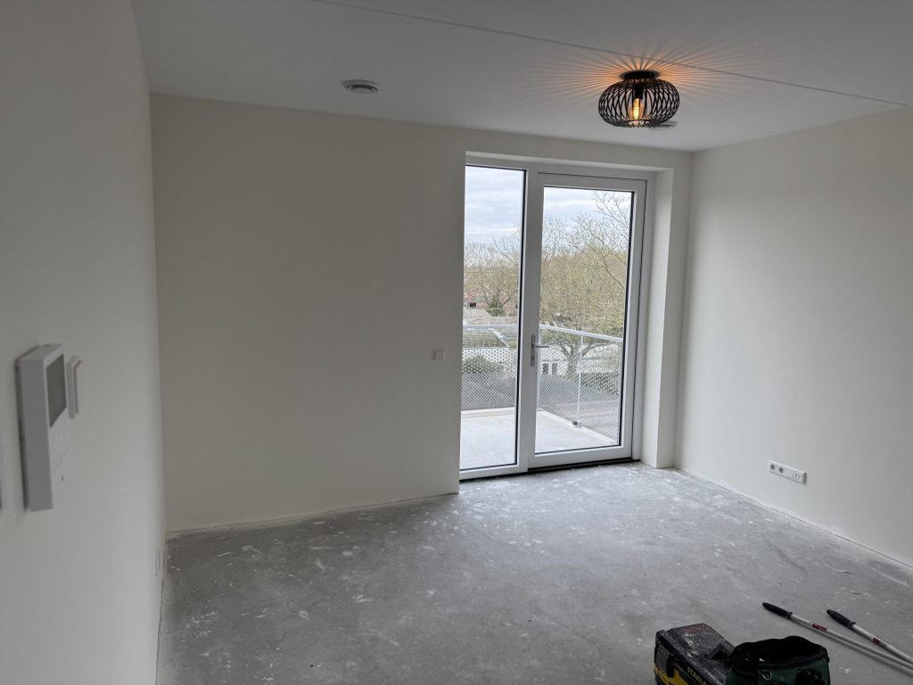 Lege kamer met lichte wanden en een balkondeur, klaar om de muren op te meten