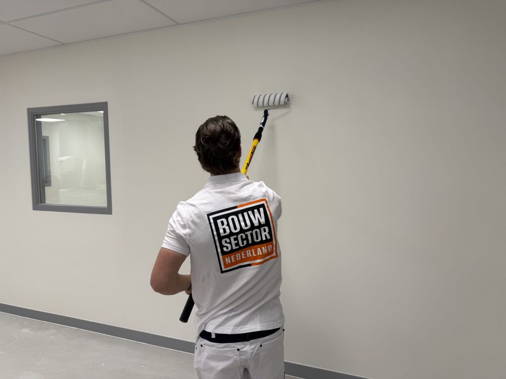 Vakman van Bouwsector Nederland rolt met een verfroller op een steel een witte sauslaag op een gladde wand