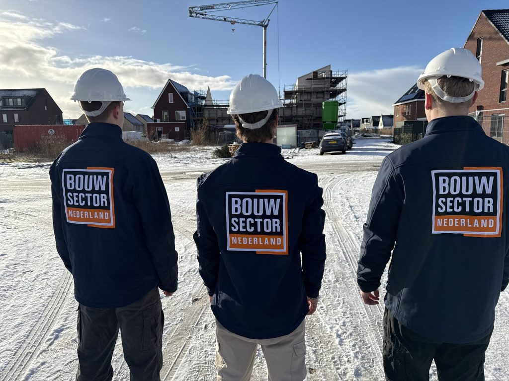 Drie vakmensen met witte helm kijken naar woningen in aanbouw